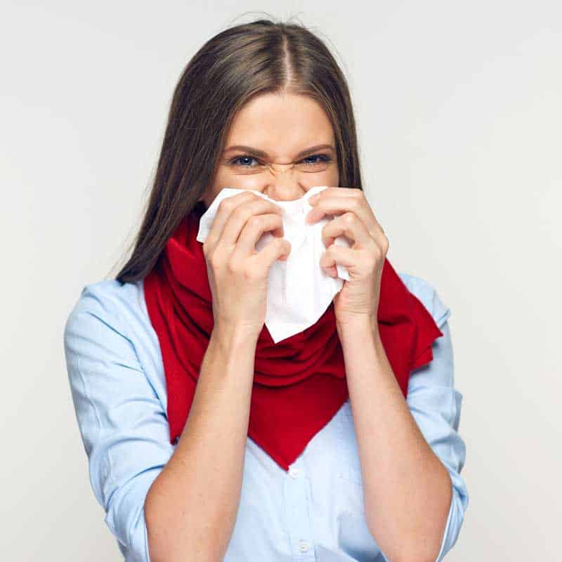 woman blowing nose in tissue suffering from seasonal allergies